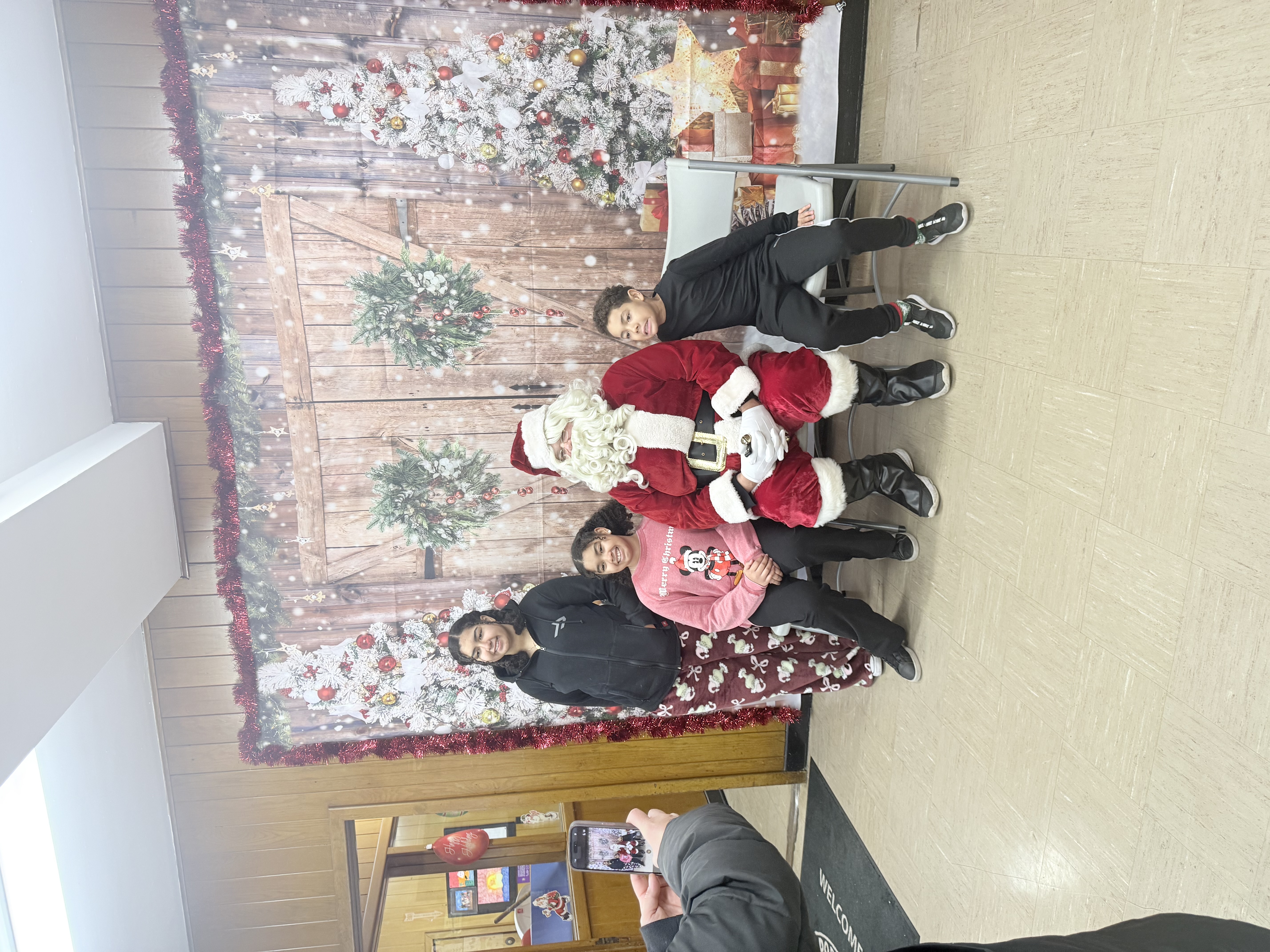 Photograph of children laying on Santa for a picture in front of a backdrop.